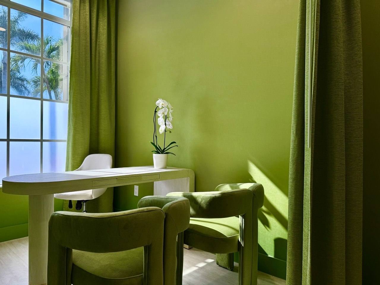 A sunlit consultation room washed in living green, a white orchid at its centre.